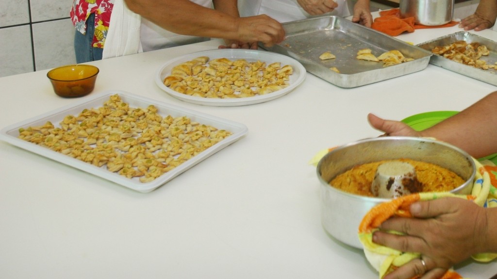a foto é fechada em mãos preparando salgados e uma mão segurando uma forma de bolo